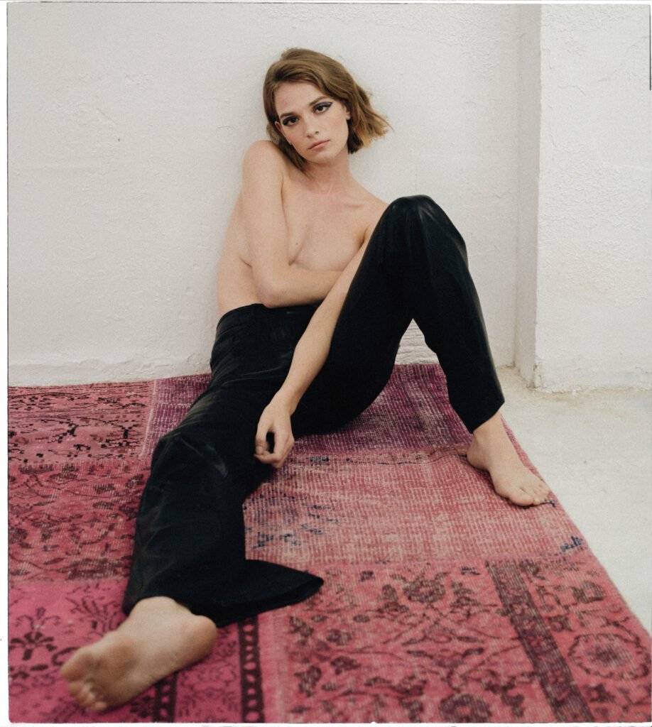 mujer con el torso cubierto por el brazo posando sentada en una alfombra