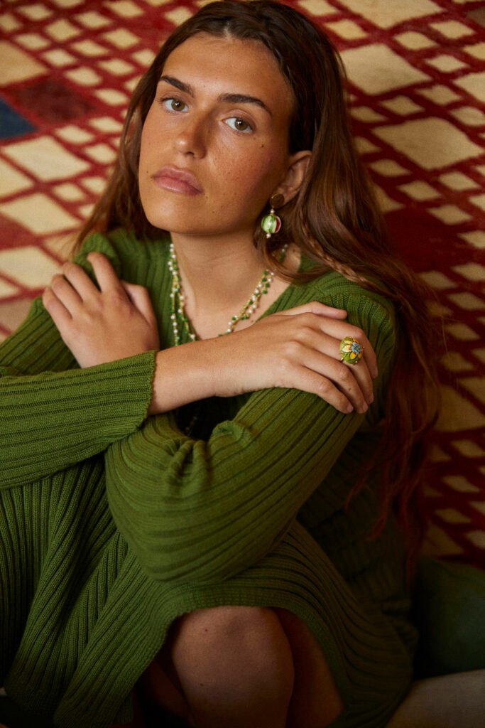 Mujer vestida de verde mirando a la camara y sentada en el suelo